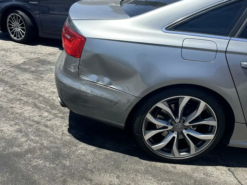 Silver Audi sedan with a deep dent in the rear quarter panel and bumper